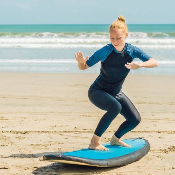 Young woman is training to stand on the surf before the first surfing lesson.