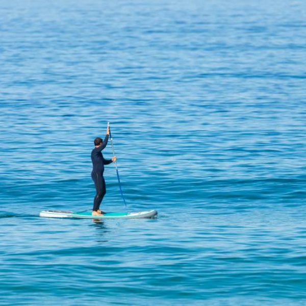 Stand up paddle boarder in wetsuit paddling on a sea. Minimalist image.